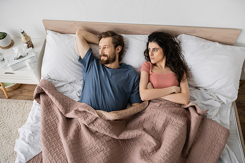 Top view of dissatisfied brunette woman looking at bearded boyfriend on bed at home