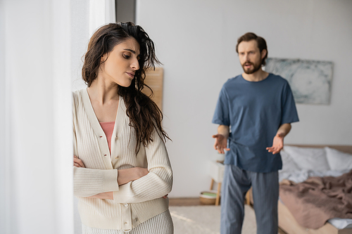 Upset woman crossing arms while blurred boyfriend quarrelling at home