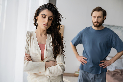 Sad woman standing near blurred boyfriend during relationship difficulties at home