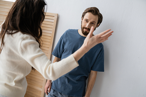 Frustrated man in pajama standing near blurred girlfriend quarrelling at home