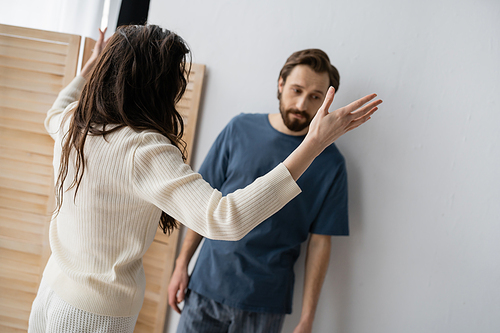 Brunette woman quarrelling at frustrated blurred boyfriend at home