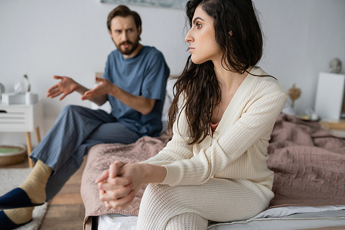 Offended woman looking away while blurred boyfriend talking in bedroom