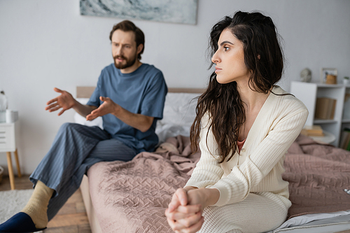 Offended woman sitting near blurred boyfriend talking during relationship difficulties at home