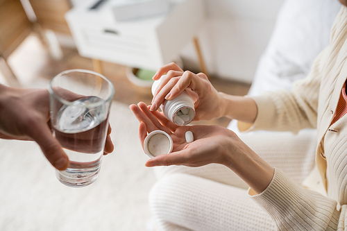 Cropped view of woman pouring pill on hand near boyfriend with glass of water at home