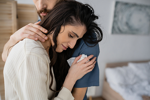 Bearded man calming sad girlfriend with napkin in blurred bedroom