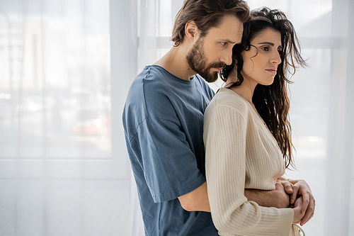 Caring bearded man embracing sad girlfriend at home