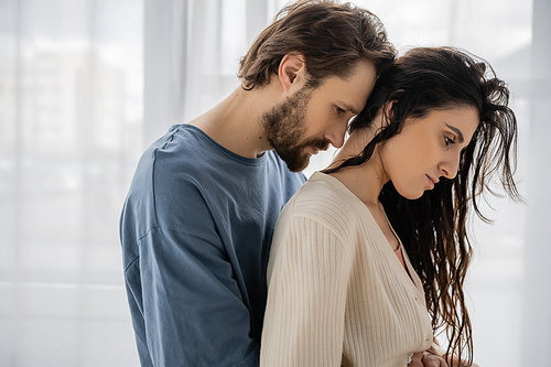 Side view of sad bearded man hugging girlfriend at home