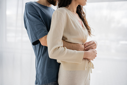 Cropped view of man in pajama embracing brunette girlfriend at home