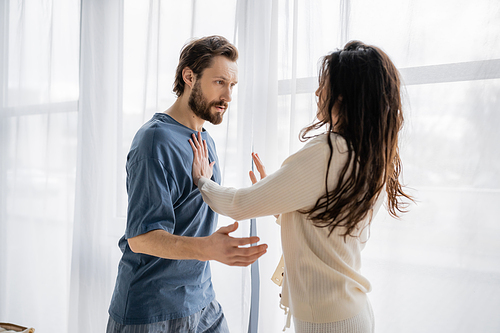 Brunette woman showing stop gesture at irritated boyfriend at home