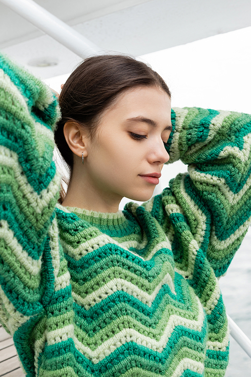 Pretty young woman in knitted sweater touching hair on yacht