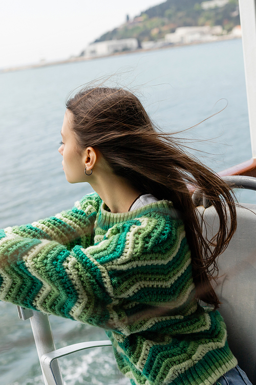 Side view of young brunette woman in knitted sweater looking at sea during cruise on yacht in Turkey