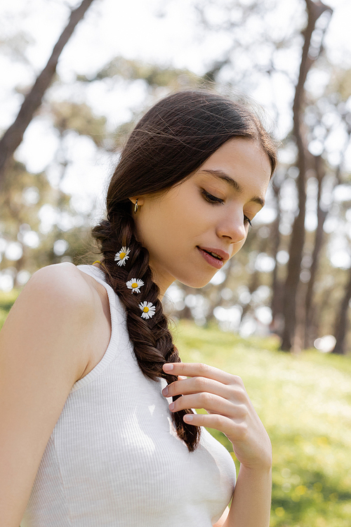 Young brunette woman touching hair with daisies in park
