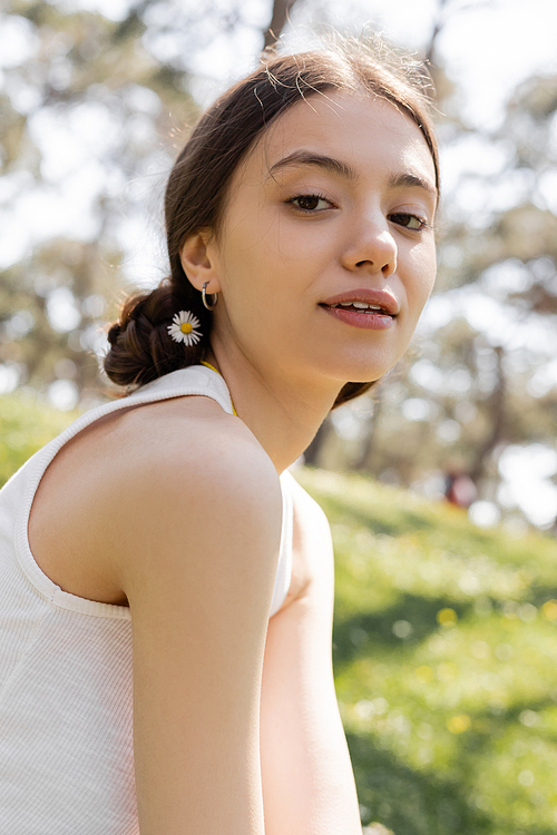 Portrait of young woman with flower in hair looking at camera in park