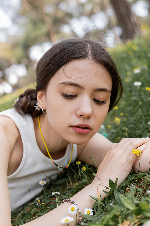 Young woman in top looking at flowers while lying on meadow in park