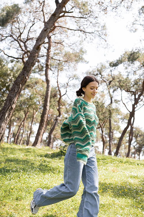 Carefree young woman in sweater and jeans walking on summer park