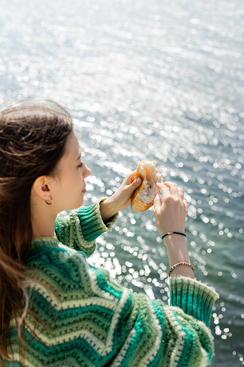 Side view of blurred brunette woman holding bread near blurred sea in Turkey