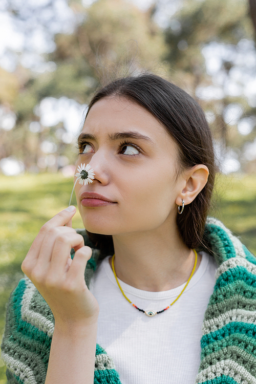 Young brunette woman smelling daisy and looking away in park