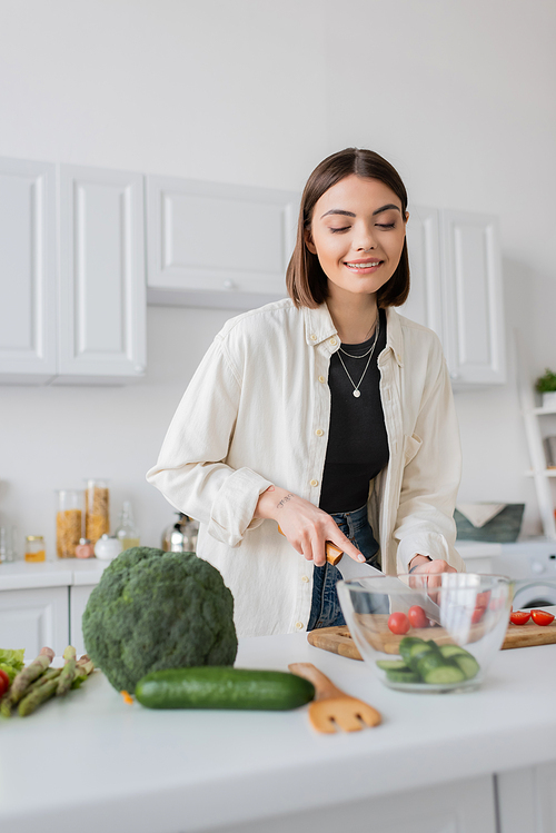 Smiling young woman cutting vegetables while cooking salad in kitchen