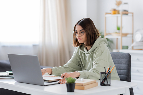 Brunette freelancer using laptop near notebooks and books at home
