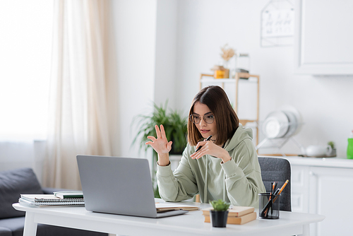 Freelancer in eyeglasses having video chat on laptop near notebooks at home