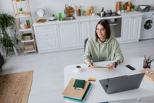 Overjoyed freelancer holding notebook near gadgets and coffee at home