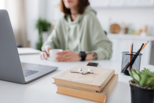 Cropped view of earphones on books near laptop and blurred freelancer at home