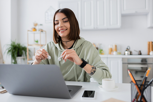 Overjoyed freelancer holding earphones near devices and coffee at home