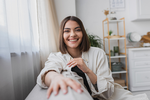 Carefree young woman looking at camera while sitting on couch at home