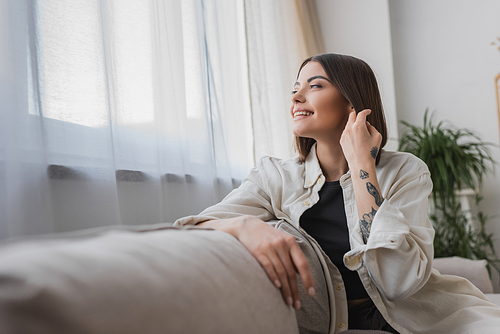 Positive young woman touching hair while sitting on couch at home