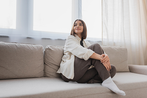Smiling young woman looking away while sitting on couch at home