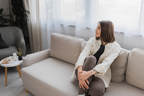 Young brunette woman smiling while sitting on couch in living room