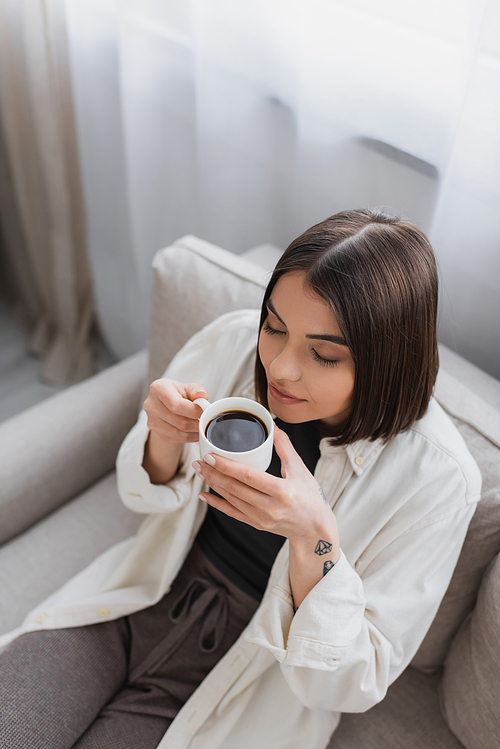 Overhead view of tattooed woman holding cup of coffee while sitting on couch