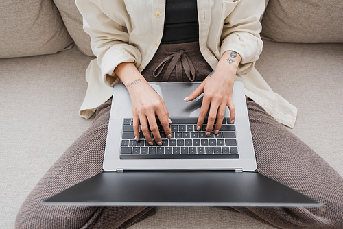 Top view of tattooed freelancer using laptop with blank screen on couch in living room