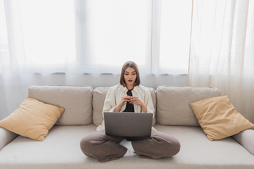 Shocked freelancer looking at laptop on couch in living room