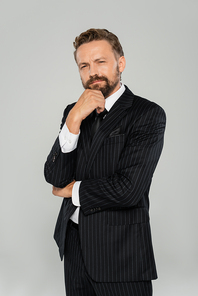 pensive and bearded man in formal wear looking at camera isolated on grey