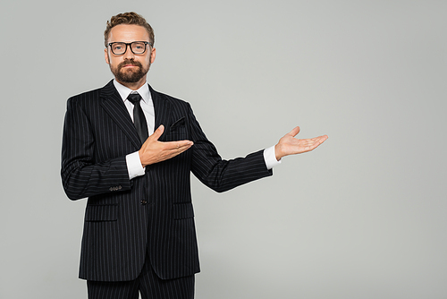 bearded businessman in formal wear and glasses pointing with hands isolated on grey