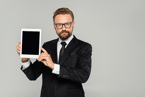 bearded businessman in formal wear and glasses holding digital tablet with blank screen isolated on grey