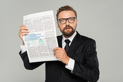 shocked businessman in suit and glasses holding newspaper isolated on grey