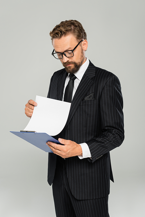 well dressed businessman in glasses holding clipboard and paper isolated on grey