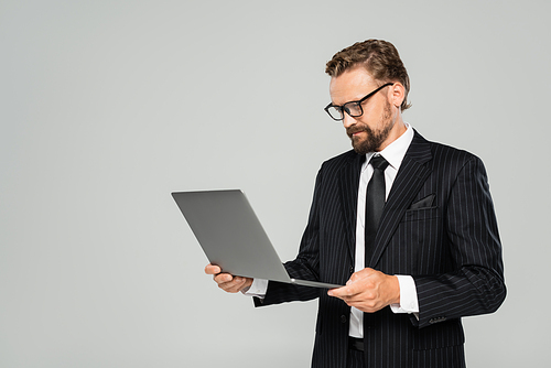 well dressed businessman in glasses using laptop isolated on grey