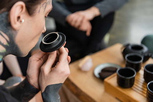 tattooed young man smelling puer tea near Chinese cups in yoga studio
