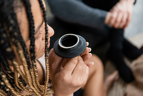 overhead view of african american woman with dreadlocks smelling puer tea from teapot lid