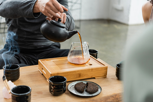 cropped view of man pouring freshly brewed puer tea into glass jug
