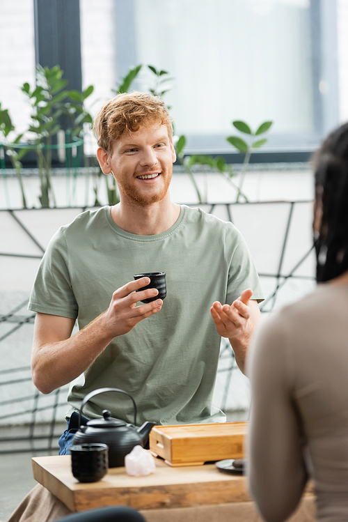 happy man with red hair and beard holding Chinese cup and talking with african american woman