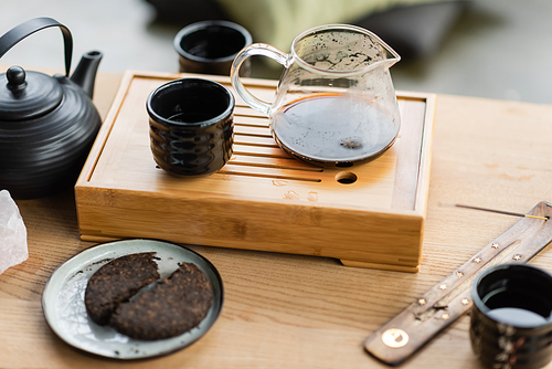 compressed pu-erh tea near Chinese teapot and incense stick on wooden stand