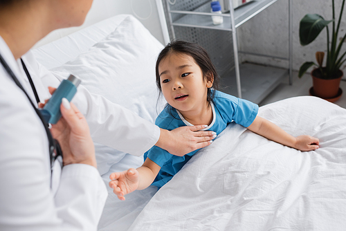 curious asian girl with outstretched hand reaching doctor with inhaler in hospital