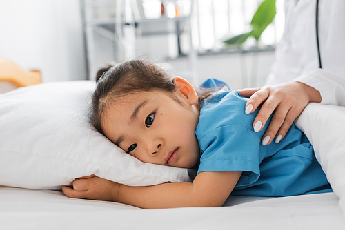 doctor calming upset asian girl lying on bed in hospital ward