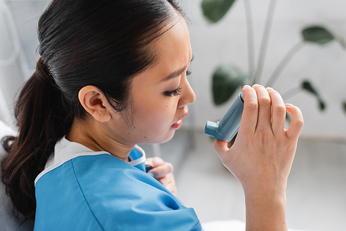 side view of diseased asian woman holding inhaler in hospital ward