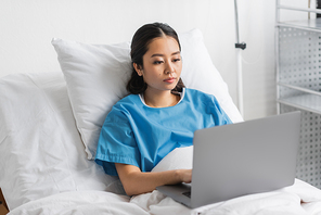 young asian woman working on laptop on bed in hospital ward