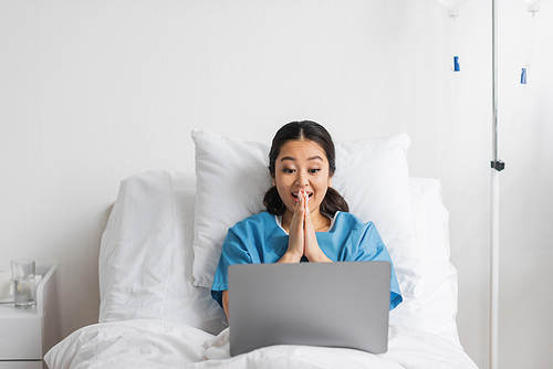 excited asian woman gesturing during video call on laptop in hospital ward